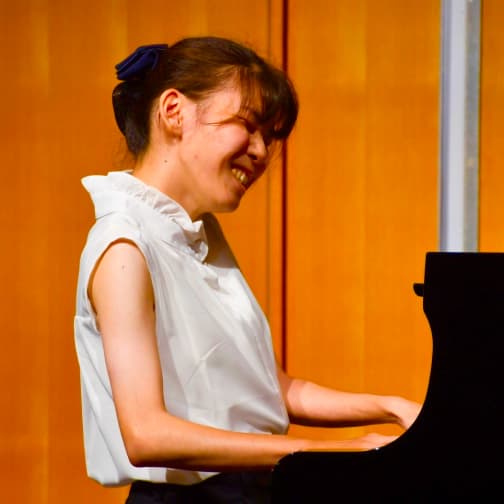 西脇有希のポートレート。白いブラウスを着て、笑顔でピアノを弾いている。